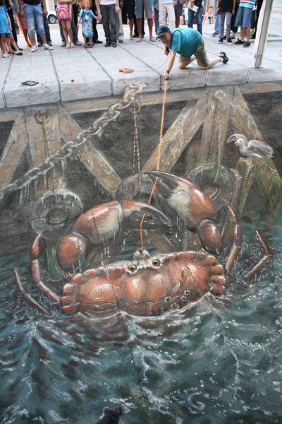 3D chalk trompel'oeil of a giant crab in water being caught by the artist