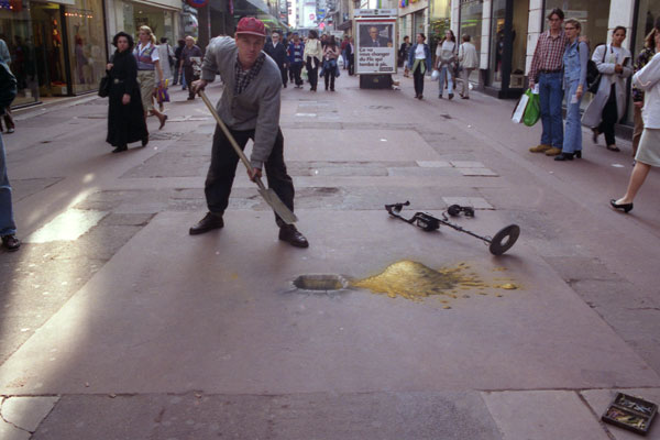 Pavement drawing of the artist Julian Beever starting to dig a hole in the street with his metal detector next to him