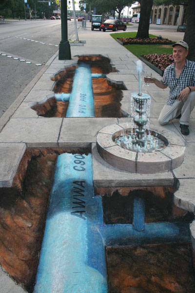 3D sidewalk drawing of underground pipes bringing water to a fountain with the artist about to drink form it