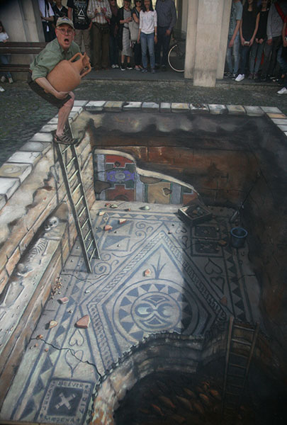 3D street art of a drawn underground archeological site with the artist Julian Beever posing trying to steal an artefact