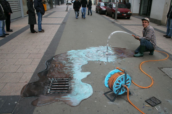 Calk trompe l'oeil of a hosepipe pouring water into a gutter, with the artist Julian Beever holding it