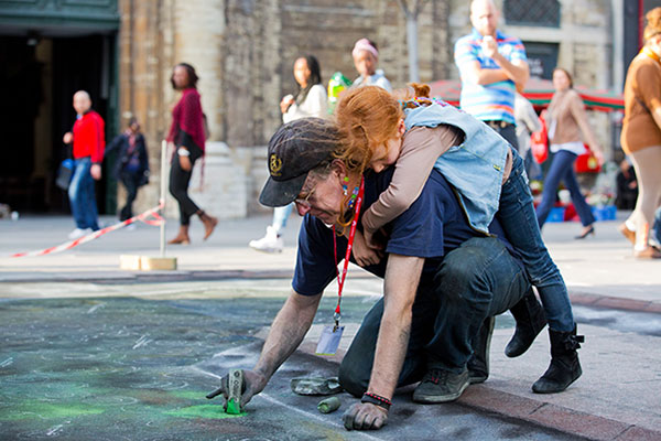The artist Julian Beever draing while his daughter is giving him a hug