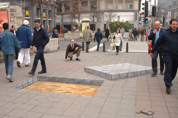 3D chalk illusion of a stack of paving slabstaken out of the ground, leaving a big hole with sand under it.