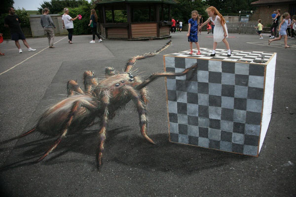 3D sidewalk chalk drawing of a giant spider about to reach two real girls posing on a drawn cube