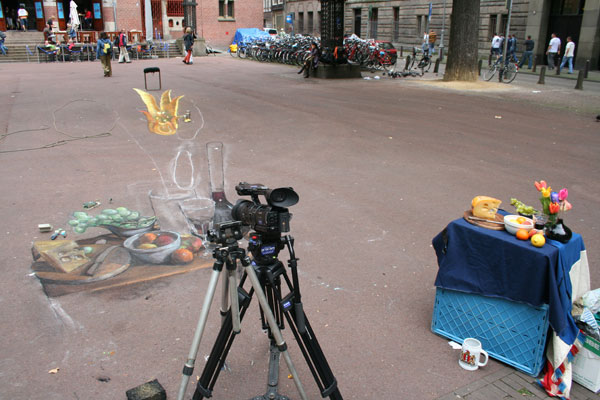 Still life 3D drawing seen distorted on the street with the real objects next to it.